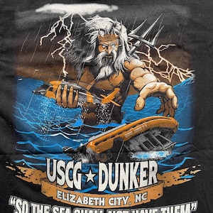 May include: Black t-shirt featuring a graphic of a muscular figure with a trident, holding a helicopter and a sinking boat in stormy waters. The text "USCG DUNKER" and "SO THE SEA SHALL NOT HAVE THEM" are displayed.