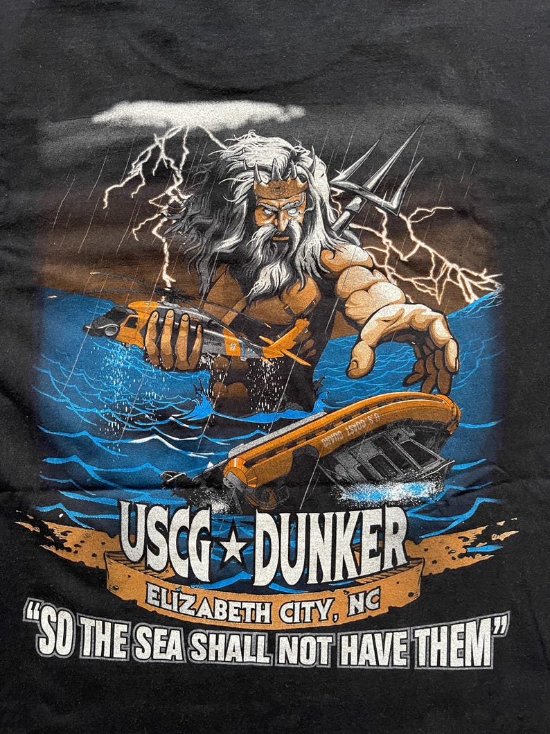 May include: Black t-shirt featuring a graphic of a muscular figure with a trident, holding a helicopter and a sinking boat in stormy waters. The text "USCG DUNKER" and "SO THE SEA SHALL NOT HAVE THEM" are displayed.