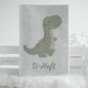 May include: A gray felt book cover with a green embroidered dinosaur and the text "U-Heft" in white embroidery.