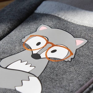 Può includere: Tessuto in pile grigio con un'applicazione grigia e bianca di una volpe con occhiali arancioni.