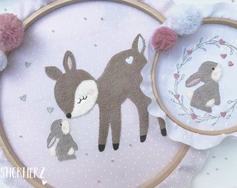 May include: Two embroidered hoop art pieces with a pink and white polka dot background. One hoop features a brown deer with closed eyes and a small brown bunny looking up at it. The other hoop features a brown bunny in a wreath of green leaves and pink hearts.