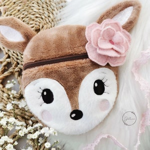 May include: A brown plush deer-shaped zippered pouch with a pink felt flower on top. The pouch has embroidered eyes and a black nose.