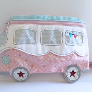 Könnte beinhalten: Ein rosa-weißer Stoff-Campingbus mit blauem Dach, Punkte-Muster und gestickten Fenstern. Der Campingbus hat einen roten Stern an jedem Rad und einen kleinen Anhänger.