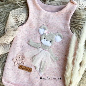 Könnte beinhalten: Ein rosa ärmelloser Strampler mit einem Ballerina-Bären-Applik. Der Strampler hat ein gesprenkeltes Muster und steht "Handmade" und "Millie & Joolz" auf der Vorderseite.