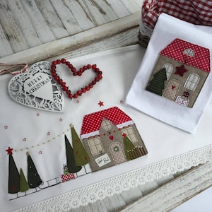 May include: White embroidered kitchen towels with a Christmas theme. One towel features a house with a red roof and a Christmas tree. The other towel features a row of houses with Christmas trees and the text "God Jul".