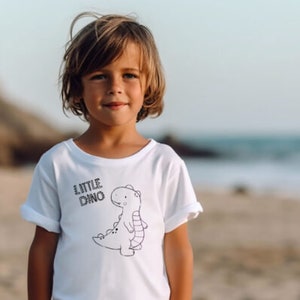 May include: A young person wearing a white t-shirt with a black and white illustration of a dinosaur and the text "Little Dino".