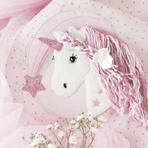 Könnte beinhalten: Ein weißer Einhornkopf mit einem rosa Glitzerhorn und einer fließenden rosa und weißen Mähne. Ein rosa Sternschnuppen mit einem Glitzerstern befindet sich neben dem Einhorn. Das Einhorn befindet sich auf einem rosa Hintergrund mit weißen Punkten.