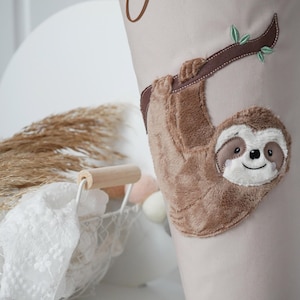 Peut inclure: Cône en tissu beige avec une application de paresseux en peluche. Le paresseux est marron avec un visage blanc et est suspendu à une branche marron avec des feuilles vertes. Le cône a un ruban marron attaché.
