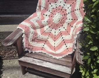May include: A handmade crochet blanket featuring a star-shaped pattern with alternating rows of cream and dusty rose yarn. The textile has a thick, textured stitch construction with a scalloped edge, creating a geometric design in soft colours.