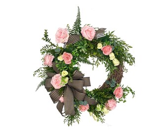 May include: A decorative wreath featuring pink roses, small white flowers, and green foliage. The wreath includes a large black and tan striped bow. The base of the wreath appears to be made of woven branches.