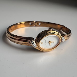 Può includere: Orologio al quarzo Lassale dorato con quadrante ovale e bianco. L'orologio presenta lancette e indici dorati ed è impreziosito da piccoli cristalli. Il cinturino è a bracciale dorato.