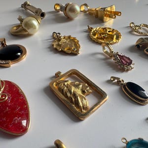 May include: A collection of gold and silver pendants with various designs, including a lion, a heart, a crown, and a stone. The pendants are on a white surface.