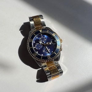 May include: A two-tone gold and silver chronograph wristwatch with a blue face and a rotating bezel. The watch has a date window at the 4 o'clock position and a Citizen logo.