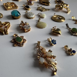 May include: A collection of gold-tone pendants with various colored stones and designs. The pendants feature a variety of shapes, including hearts, stars, and flowers. Some pendants have a single stone, while others have multiple stones. The pendants are all made of metal and have a shiny finish.