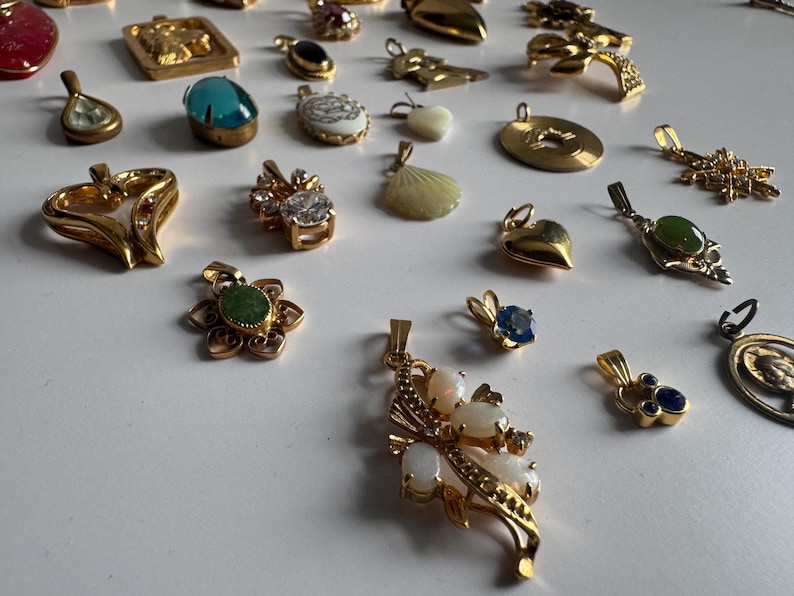 May include: A collection of gold-tone pendants with various colored stones and designs. The pendants feature a variety of shapes, including hearts, stars, and flowers. Some pendants have a single stone, while others have multiple stones. The pendants are all made of metal and have a shiny finish.