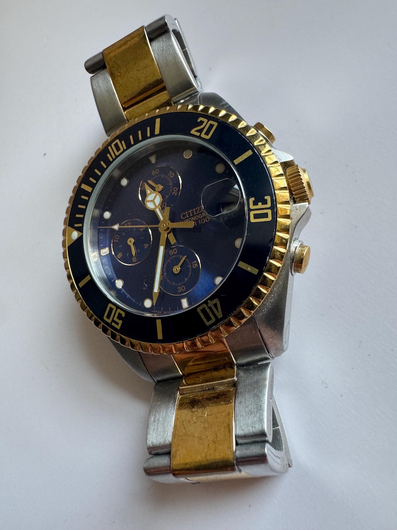 May include: A two-tone gold and silver Citizen Eco-Drive chronograph wristwatch with a black face and a rotating bezel.