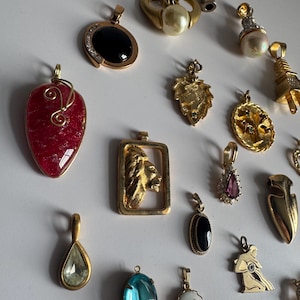 May include: A collection of gold-tone pendants with various gemstones and designs, including a heart-shaped pendant with a red stone, a lion pendant, a pendant with a blue stone, and a pendant with a pearl.