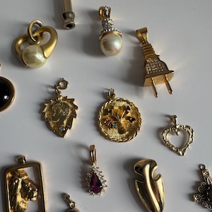 May include: A collection of 15 gold-tone charms, including a lion, a heart, a tree, a plug, and a whistle. The charms are all different sizes and shapes and have various embellishments, such as rhinestones, pearls, and enamel.