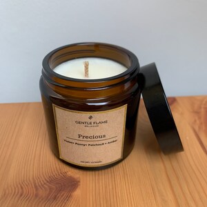 Peut inclure: Un bocal en verre brun avec un couvercle noir. La bougie est étiquetée "Gentle Flame Belgium" et "Precious" avec les notes de parfum "Violette, pivoine, patchouli, ambre". La bougie est de 130 ml et a une durée de combustion de 45 heures.