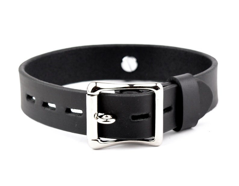 K&ouml;nnte beinhalten: Schwarzes Lederhalsband mit einer silbernen Schnalle und einem einzigen Loch oben. Das Halsband ist an den R&auml;ndern vern&auml;ht und hat eine Reihe von L&ouml;chern zum Einstellen der Gr&ouml;&szlig;e.