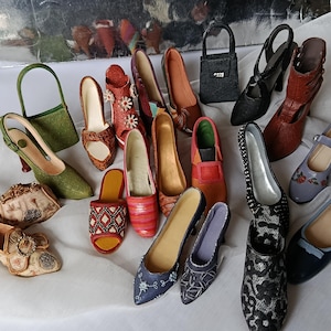 Könnte beinhalten: Eine Sammlung von Miniatur-Schuhen und Handtaschen in verschiedenen Stilen und Farben. Das Sortiment umfasst High Heels, Ballerinas und Sandalen mit Details wie Blumenmustern, Verzierungen und unterschiedlichen Texturen. Eine kleine grüne Handtasche ist ebenfalls vorhanden.