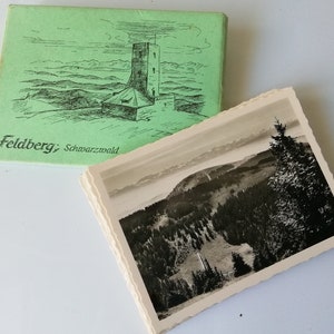 Könnte beinhalten: Ein Vintage-Postkartenset mit einem Schwarzweißfoto einer Bergkette mit einem Turm in der Ferne. Die Postkartenhülle ist grün und zeigt eine Strichzeichnung des Turms.