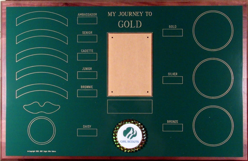May include: A green wooden plaque with gold lettering and a gold Girl Scouts emblem. The plaque has spaces for patches and awards for each level of Girl Scouts, from Daisy to Ambassador. The text on the plaque reads "My Journey to Gold".