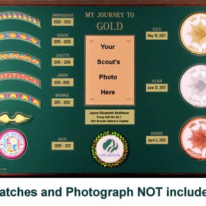 May include: Green wooden plaque with a gold frame, displaying a Girl Scout Journey to Gold award chart. The chart includes a space for a photo, a list of levels, and dates for each level. The plaque also features a Girl Scout logo and the words "My Journey to Gold".