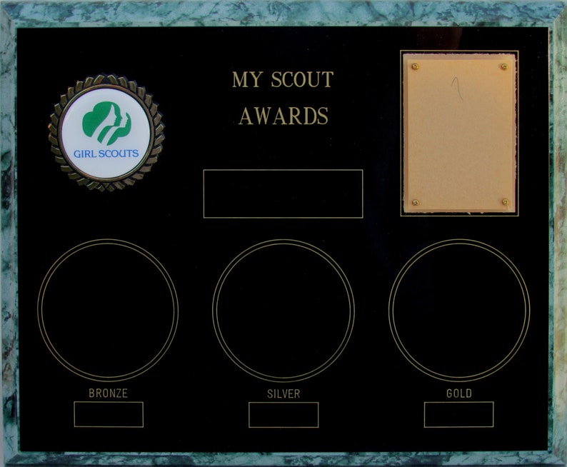 May include: A black plaque with a green marble border. The plaque has a Girl Scouts logo, the text "MY SCOUT AWARDS", and three blank circles labeled "BRONZE", "SILVER", and "GOLD".