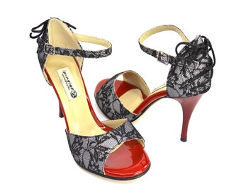 May include: A pair of black lace heeled sandals with red patent leather accents. The sandals have a delicate lace design and a thin ankle strap. The brand name "imagine" is printed on the insole.
