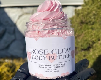 May include: A pink rose-scented body butter in a clear jar with a white label that reads "ROSE GLOW BODY BUTTER" and "MADE WITH NOURISHING ALMOND OIL AND SHEA BUTTER NET WT 6 OZ".