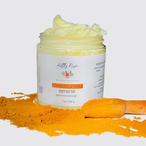 May include: A clear plastic jar filled with pale yellow body butter, topped with a swirl. The white label reads Kathy Rose, Turmeric & Shea Body Butter, 7 oz | 200 g. A wooden scoop rests in a pile of bright orange turmeric powder.