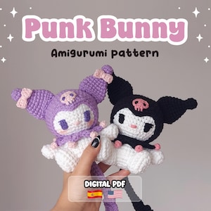 May include: Two crocheted amigurumi bunny dolls with pointed ears, one in purple and one in black, both featuring white faces, pink skull accents, and small bows. The text reads Punk Bunny Amigurumi pattern and DIGITAL PDF with Spanish and American flags.