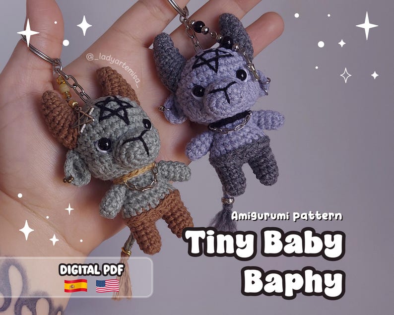 May include: Two crocheted Tiny Baby Baphy keychains. One is gray and brown, the other is gray and purple. Each has a pentagram on its head and a chain collar. The keychains are attached to silver keyrings.