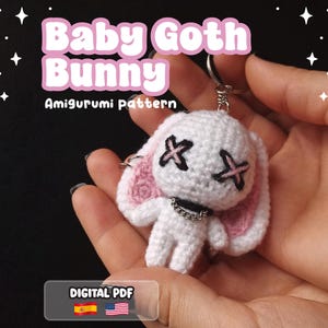 Puede incluir: Un llavero de conejo amigurumi de ganchillo blanco con orejas interiores rosas, ojos negros en forma de X y un collar de cadena plateado. El texto Baby Goth Bunny Amigurumi pattern y DIGITAL PDF es visible junto a iconos de estrellas.
