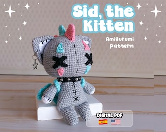 Może przedstawiać: Szara szydełkowa lalka amigurumi w kształcie kotka z czarnymi oczami w kształcie litery X, czarną obrożą z ćwiekami oraz różowymi i niebieskimi akcentami. Tekst głosi Sid, the Kitten Amigurumi pattern i DIGITAL PDF. Posiada małą zawieszkę w kształcie gwiazdki.