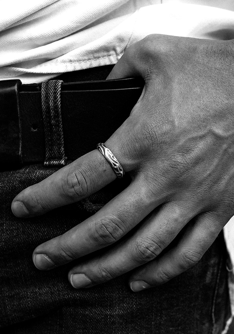 Puede incluir: Un anillo de plata con un dise&ntilde;o texturizado y org&aacute;nico. El anillo se lleva en el dedo de una persona que lleva pantalones vaqueros.