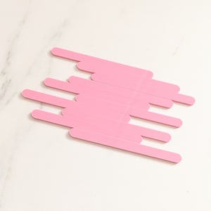 May include: A set of pink nail files arranged in a staggered pattern on a white marble surface.