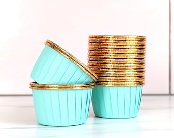 May include: A stack of light blue cupcake cases with gold foil rims. The cases are stacked on a white surface.