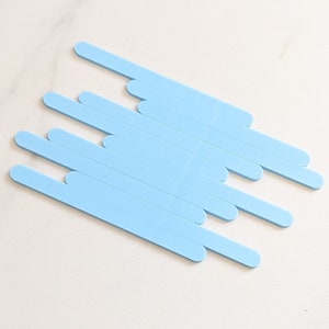 May include: A set of eight light blue plastic craft sticks. The sticks are arranged in a staggered pattern.