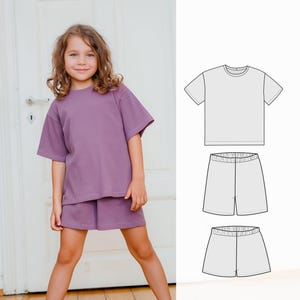 May include: A young girl wearing a lavender ribbed knit t-shirt and matching shorts. The outfit has a relaxed fit. A technical drawing of a t-shirt and shorts set is shown on the right.