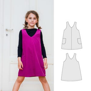 Op de afbeelding: Een magentakleurige, mouwloze jurk met een V-hals en twee zakken. Naast het meisje dat de jurk draagt, is een lijntekening van de jurk te zien.