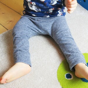 May include: A child wearing blue and white patterned pants with a blue and white patterned shirt. The child is sitting on a gray rug with a green and blue design.