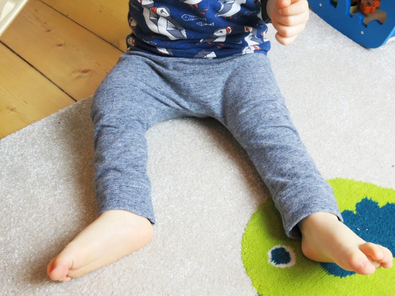 May include: A child wearing blue and white patterned pants with a blue and white patterned shirt. The child is sitting on a gray rug with a green and blue design.