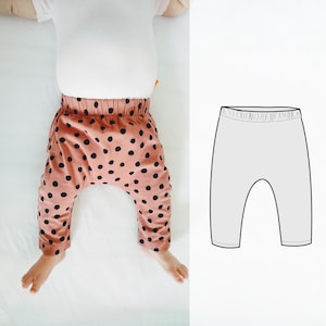Könnte beinhalten: Babyhose mit rosa Hintergrund und schwarzen Tupfen. Die Hose hat einen elastischen Bund und wird an einem Baby gezeigt. Eine Strichzeichnung der Hose befindet sich auf der rechten Seite des Bildes.