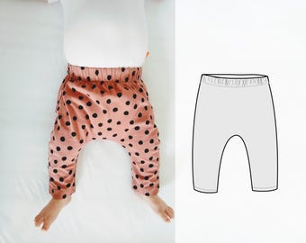 May include: Baby pants with a pink background and black polka dots. The pants have an elastic waistband and are shown on a baby. A line drawing of the pants is on the right side of the image.