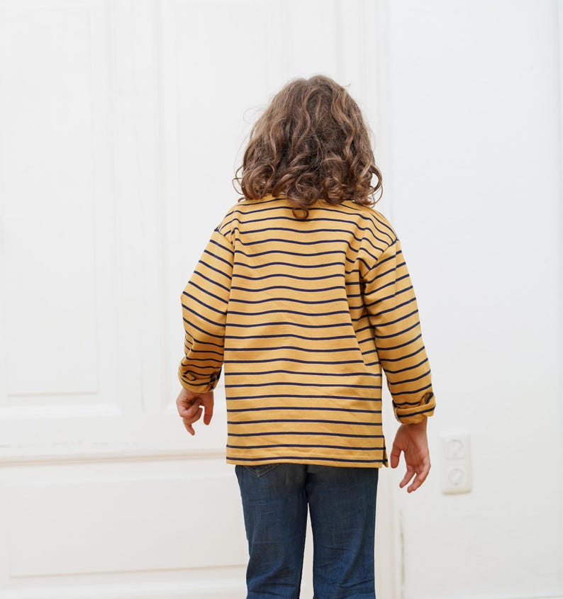 Puede incluir: Un ni&ntilde;o con una camisa de manga larga a rayas amarillas y azul marino y pantalones vaqueros azules.