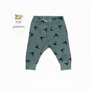 Puede incluir: Un par de leggings de bebé de color verde con un patrón de triángulos negros. Las leggings tienen una cintura elástica y tobillos con puños.