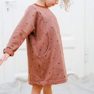 May include: A brown long-sleeved dress with a geometric pattern and a single pocket on the left side.