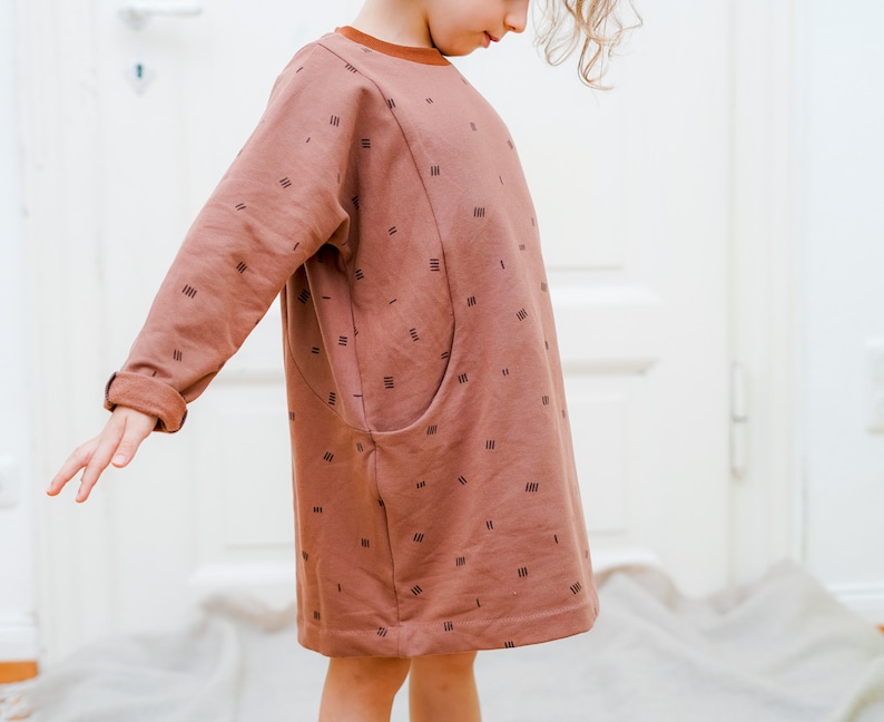 May include: A brown long-sleeved dress with a geometric pattern and a single pocket on the left side.